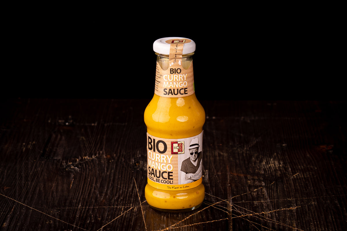 Bio-Curry-Mango-Sauce in der Glasflasche auf einem dunklen Holztisch