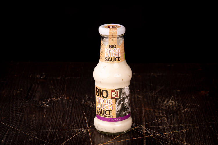 Bio-Knoblauch-Sauce in der Glasflasche auf einem dunklen Holztisch